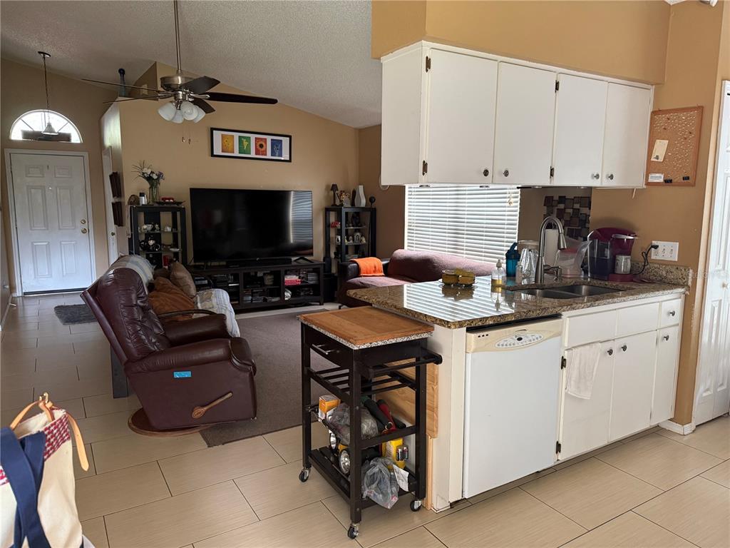 An open-concept living room and kitchen featuring tile flooring, white cabinetry, and a granite countertop — 310 PRINCE STREET, ORLANDO, FL