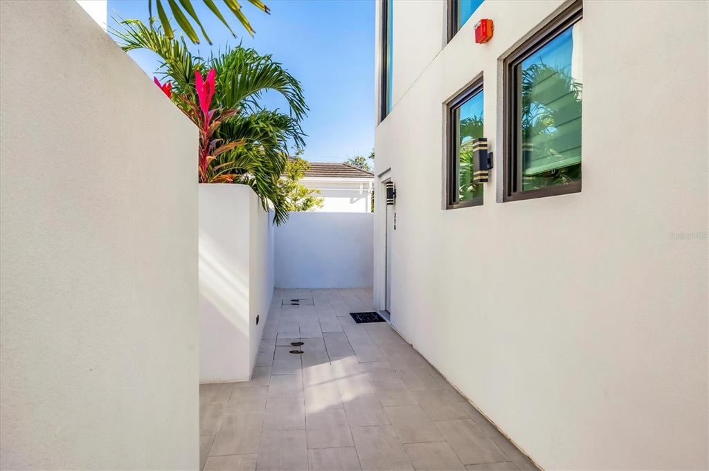 A narrow outdoor walkway paved with light tiles runs between a white wall and a building — 1558 4TH STREET UNIT 216, SARASOTA, FL