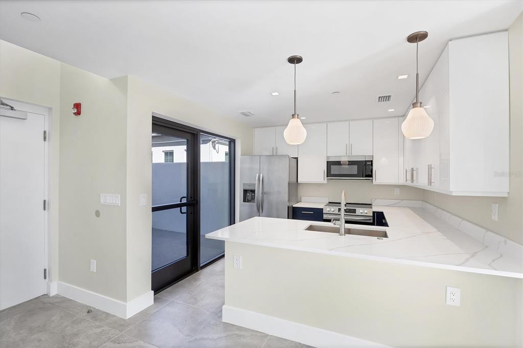 A modern kitchen features white cabinets, stainless steel appliances, and a quartz peninsula countertop — 1558 4TH STREET UNIT 216, SARASOTA, FL