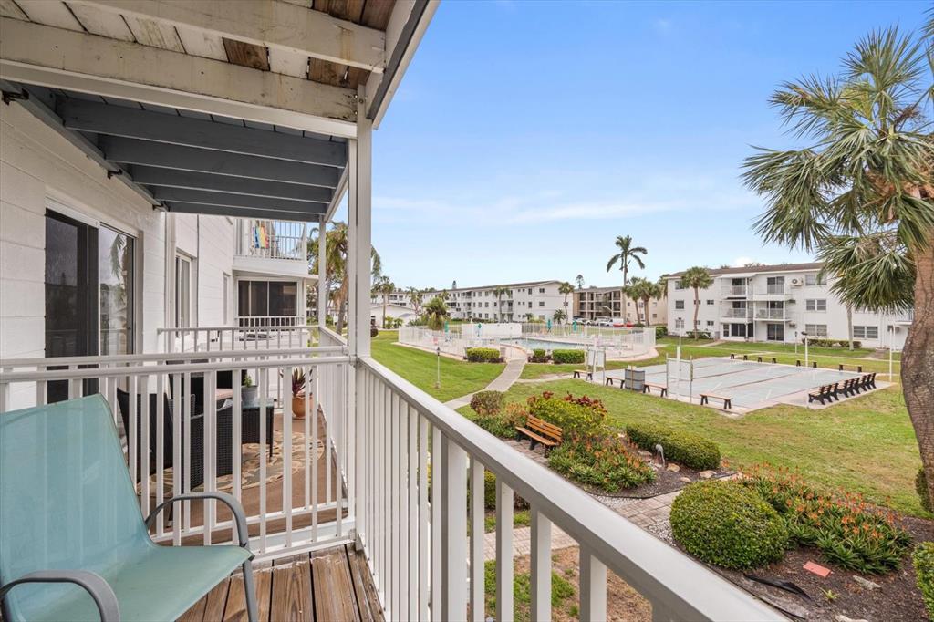 A balcony with a teal chair overlooks a grassy courtyard with a pool and tennis court — 2326 CANAL DRIVE UNIT G25, BRADENTON, FL