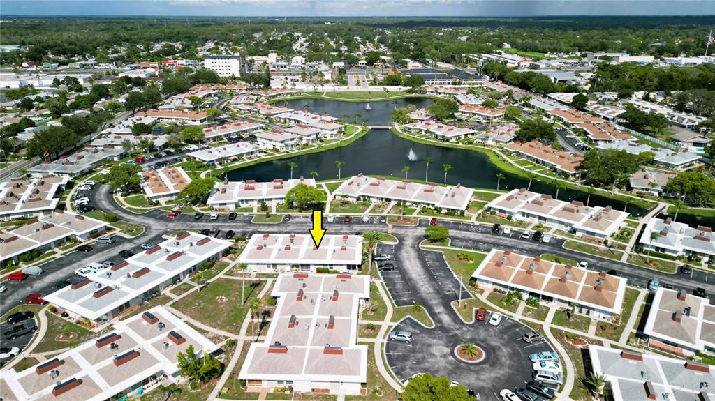 An aerial view shows a residential complex with multiple single-story buildings surrounding a central lake — 4349 TAHITIAN GARDENS CIRCLE UNIT G, HOLIDAY, FL
