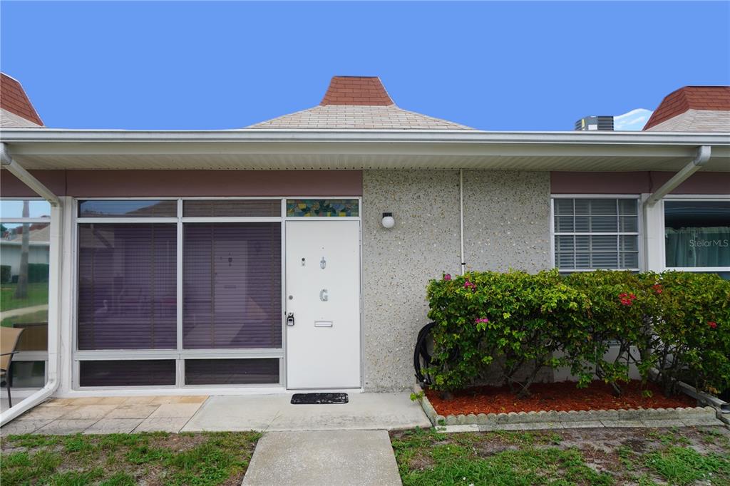The exterior of a single-story home features a white front door and a large window — 4349 TAHITIAN GARDENS CIRCLE UNIT G, HOLIDAY, FL