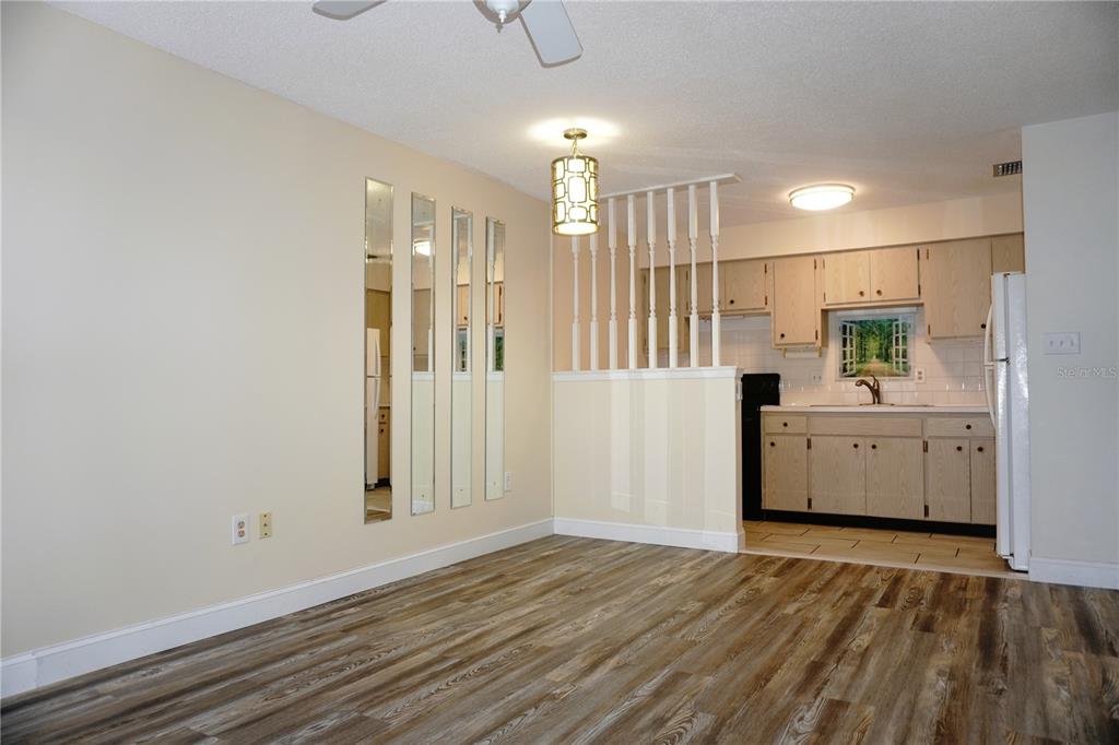 A dining area with wood-look flooring, a mirrored wall, and a half-wall partition to the kitchen — 4349 TAHITIAN GARDENS CIRCLE UNIT G, HOLIDAY, FL