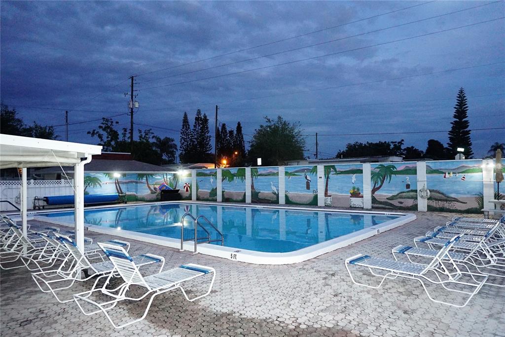 An outdoor swimming pool is surrounded by lounge chairs and a mural-painted wall at dusk — 4349 TAHITIAN GARDENS CIRCLE UNIT G, HOLIDAY, FL