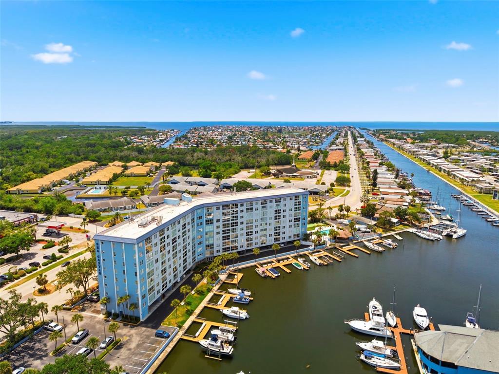 An aerial view shows a multi-story apartment building situated along a canal with docked boats — 4939 FLORAMAR TERRACE UNIT 501, NEW PORT RICHEY, FL