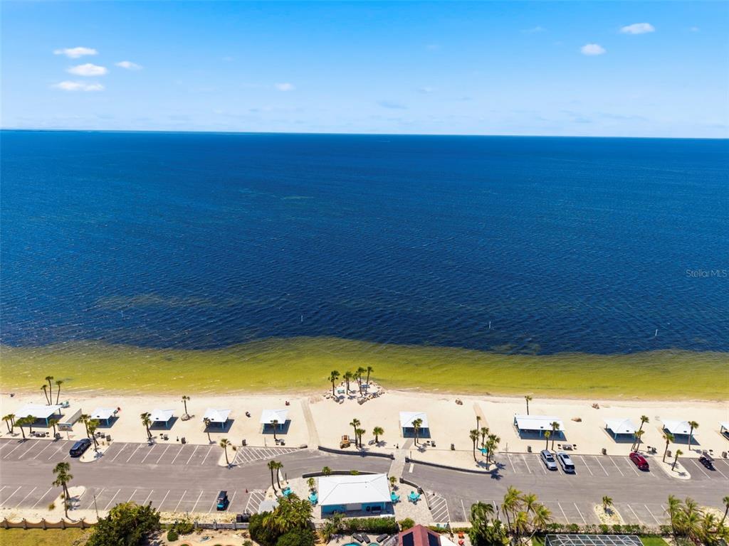 An aerial view shows a sandy beach with cabanas and a parking lot beside the ocean — 4939 FLORAMAR TERRACE UNIT 501, NEW PORT RICHEY, FL