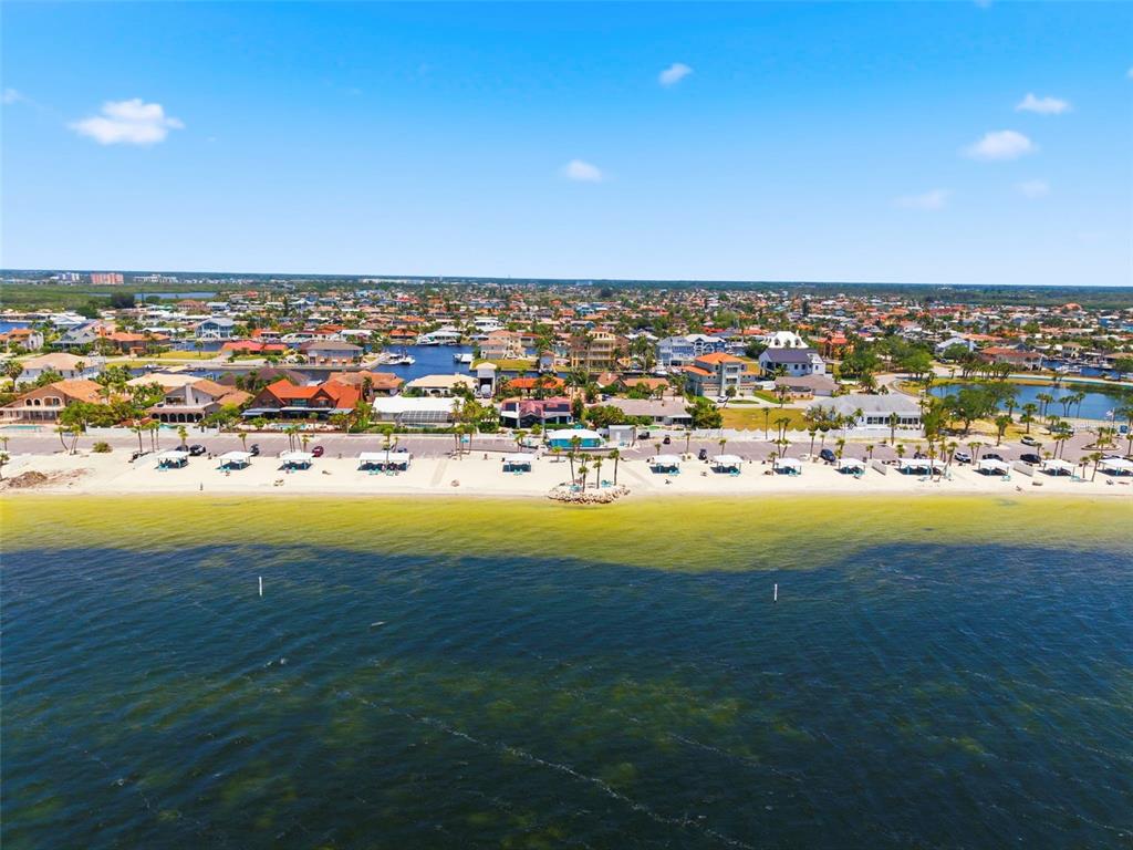 An aerial view shows a sandy beach with cabanas bordering a residential waterfront community — 4939 FLORAMAR TERRACE UNIT 501, NEW PORT RICHEY, FL