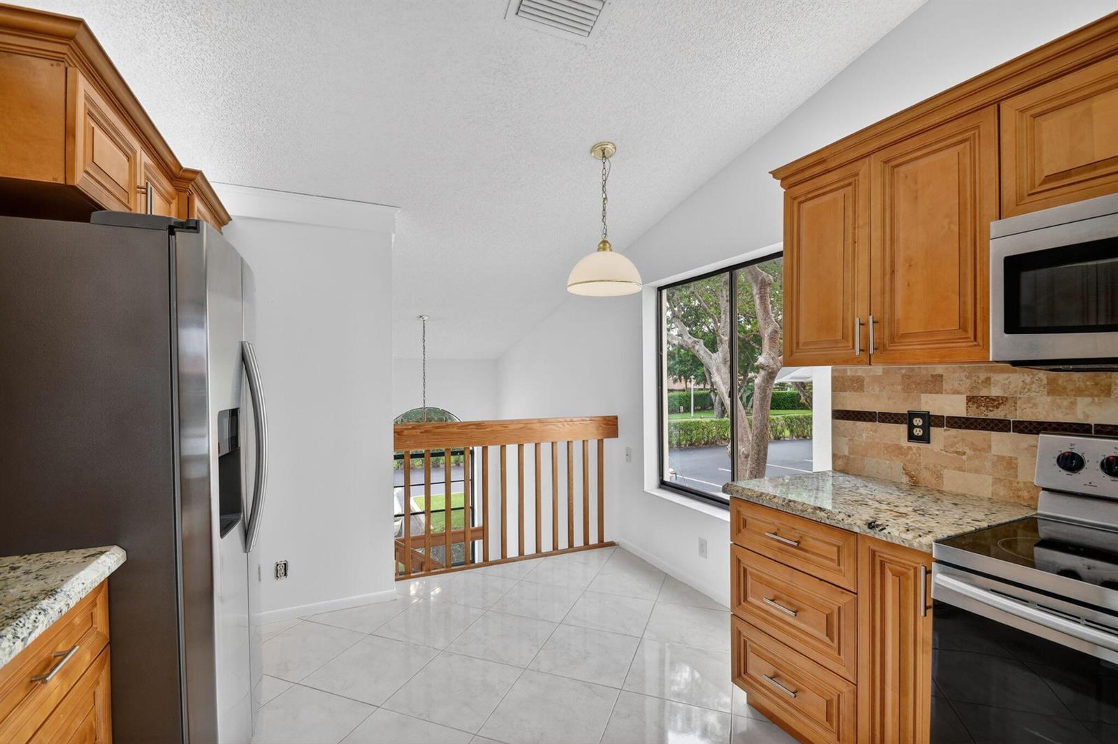 A kitchen with wood cabinets, granite countertops, and a view of trees through a window — 10231 N Circle Lake Drive # 201, Boynton Beach FL 33437, BOYNTON BEACH, FL