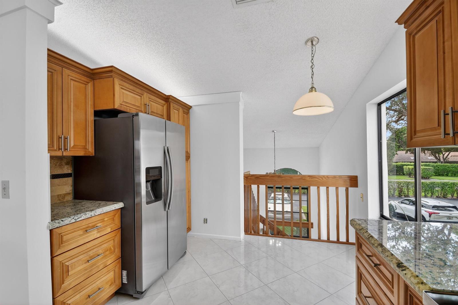 A kitchen with wood cabinets, granite countertops, and a stainless steel refrigerator overlooking a staircase — 10231 N Circle Lake Drive # 201, Boynton Beach FL 33437, BOYNTON BEACH, FL