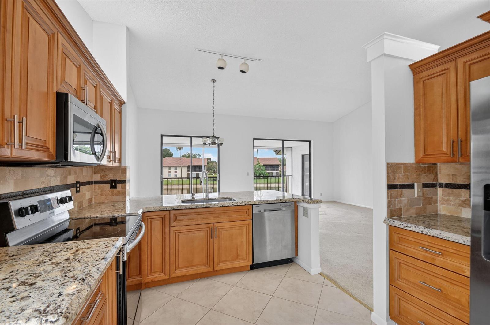 A kitchen with wood cabinets, granite countertops, and stainless steel appliances overlooks a living area — 10231 N Circle Lake Drive # 201, Boynton Beach FL 33437, BOYNTON BEACH, FL