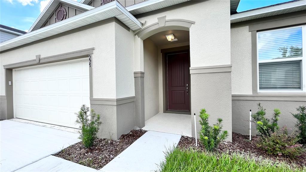 The exterior of a house features a white garage, a dark front door, and landscaping — 557 SCOTT LAKE CREEK LANE, LAKELAND, FL