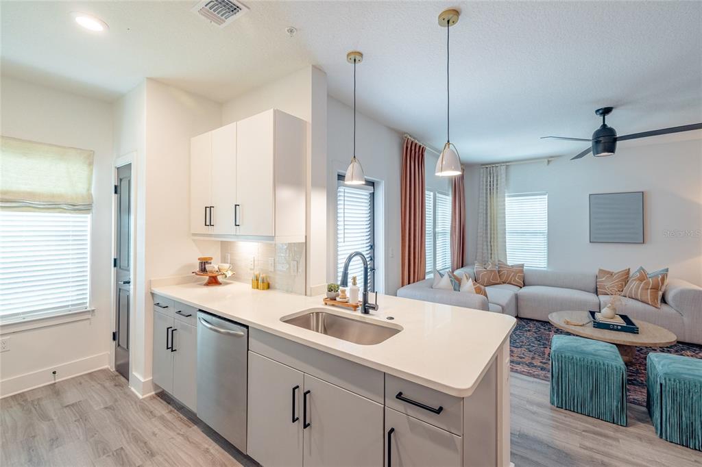 A kitchen with gray cabinets and white countertops overlooks a living room with a sofa — 1420 LAKEFRONT DRIVE UNIT 1208, SARASOTA, FL