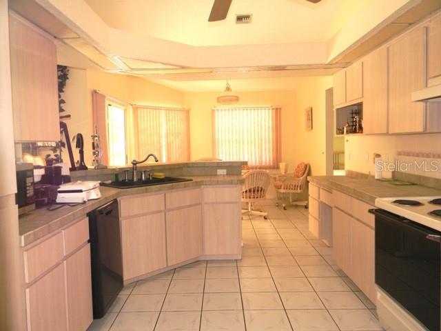A kitchen with light wood cabinets, tile flooring, and a view into a sunlit dining area — 212 BOA VISTA STREET, PUNTA GORDA, FL