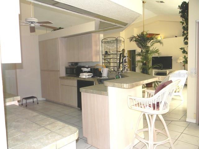 A kitchen with light wood cabinets, tiled countertops, and a breakfast bar with wicker stools — 212 BOA VISTA STREET, PUNTA GORDA, FL