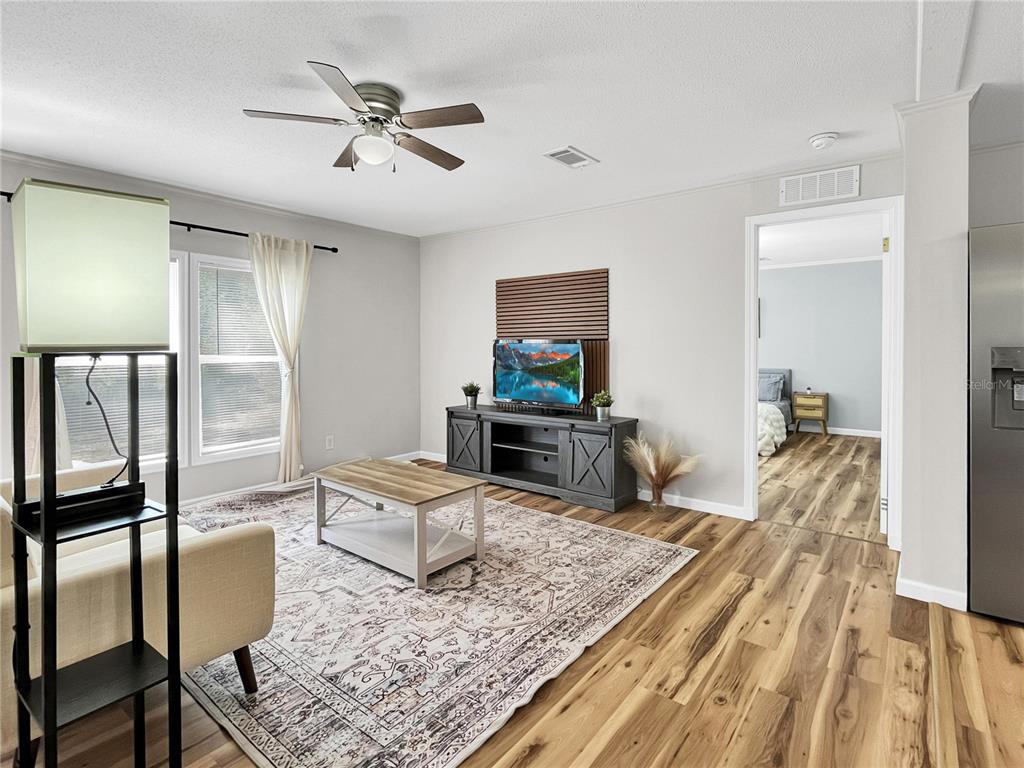 A living room features wood-look flooring, a ceiling fan, a television console, and a rug — 276 NW BATTLE HILL LANE, LAKE CITY, FL