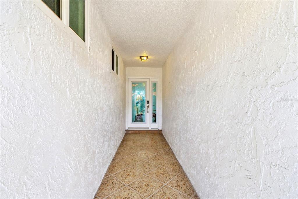 A narrow, covered entryway features white textured walls, tiled flooring, and a glass-paneled front door — 7410 8TH AVENUE W, BRADENTON, FL