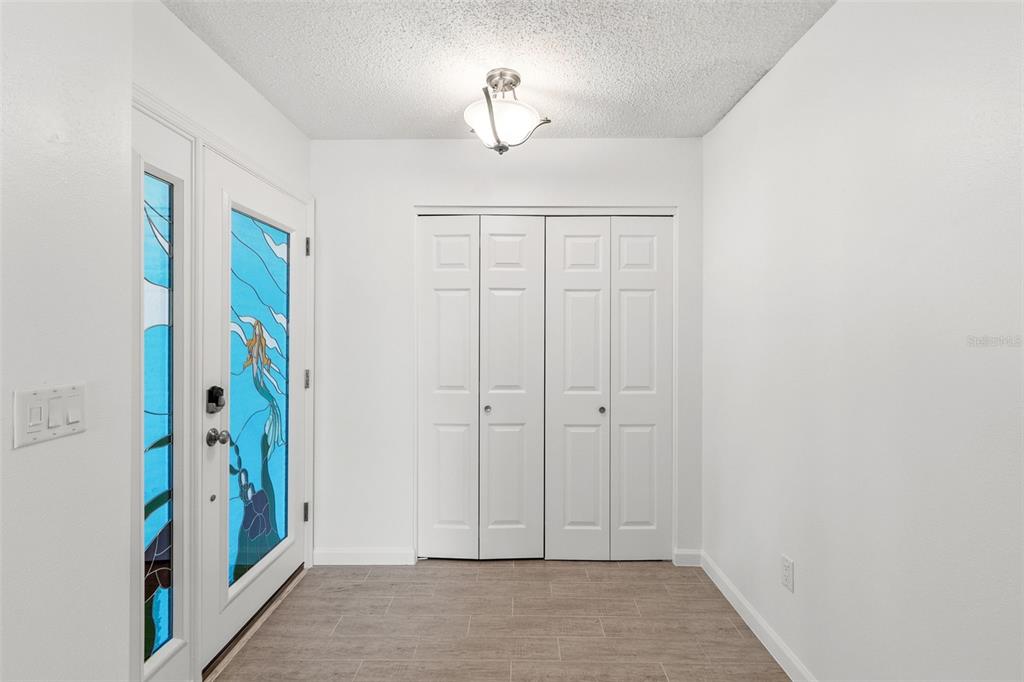 An entryway features a white door with stained glass, a closet, and light-colored tile flooring — 7410 8TH AVENUE W, BRADENTON, FL