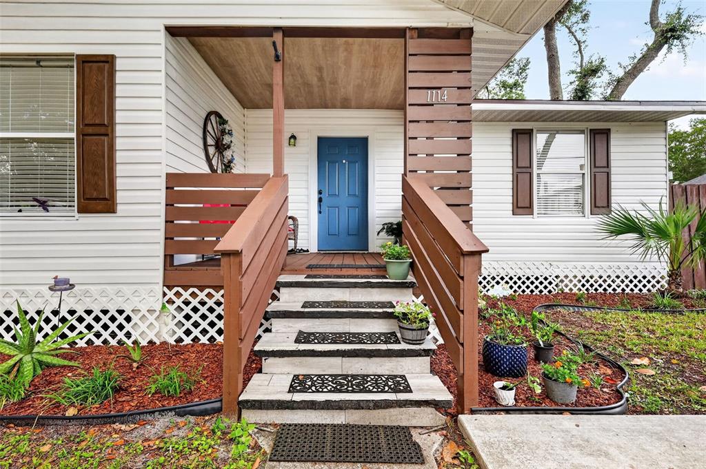 A white house exterior features a blue front door, wooden railings, and concrete steps — 1114 PINE AVENUE, SANFORD, FL