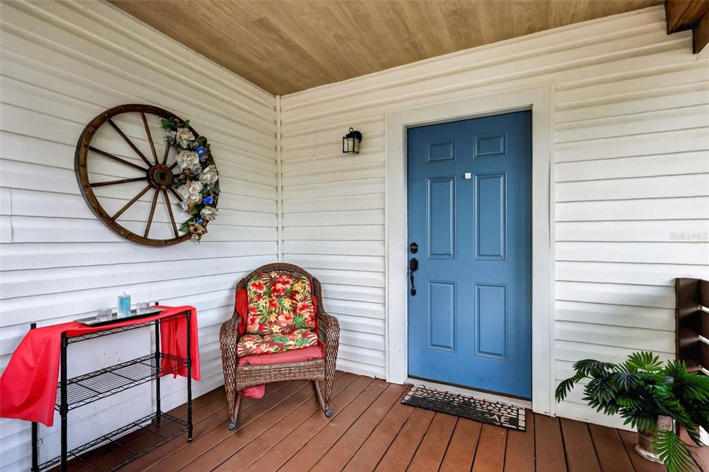 A covered porch features white siding, a blue front door, a wicker chair, and decor — 1114 PINE AVENUE, SANFORD, FL