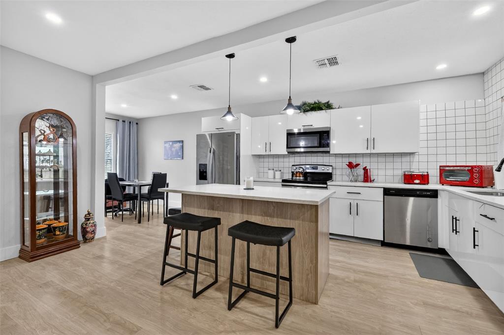 A modern kitchen features white cabinets, a wood-toned island with two stools, and stainless appliances — 1114 PINE AVENUE, SANFORD, FL
