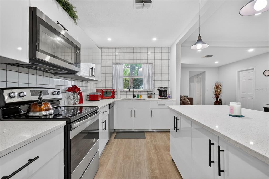 A modern kitchen features white cabinets, quartz countertops, a black stove, and white tile backsplash — 1114 PINE AVENUE, SANFORD, FL