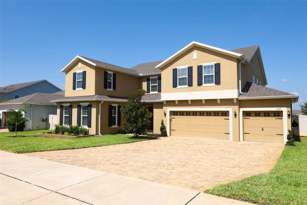 A two-story suburban house with a tan stucco exterior, dark shutters, and a paved driveway — 1329 WILDCAT LANE, MINNEOLA, FL