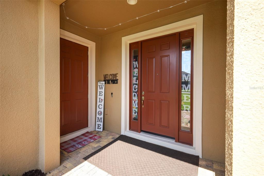 A covered entryway features a red front door, a side door, and welcome signage — 1329 WILDCAT LANE, MINNEOLA, FL