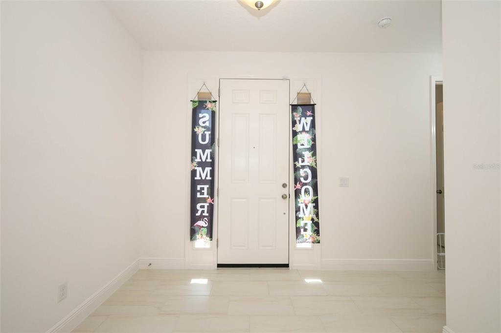 An entryway features white walls, light-colored tile flooring, and two vertical banners flanking the door — 1329 WILDCAT LANE, MINNEOLA, FL