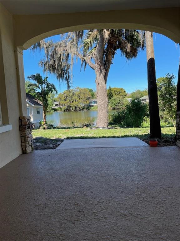 A covered patio overlooks a grassy yard, a large tree, and a lake — 5736 COLONIAL DRIVE, NEW PORT RICHEY, FL