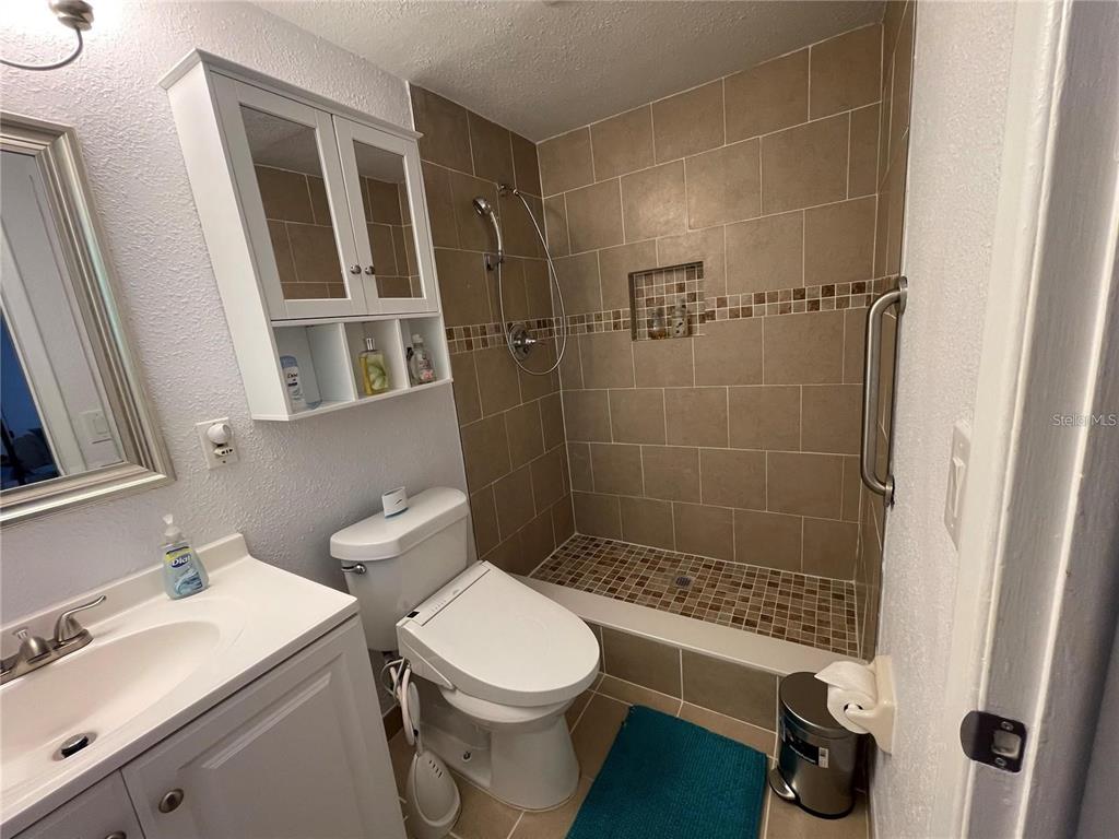 A bathroom features a white vanity, a toilet with a bidet, and a tiled walk-in shower — 5736 COLONIAL DRIVE, NEW PORT RICHEY, FL