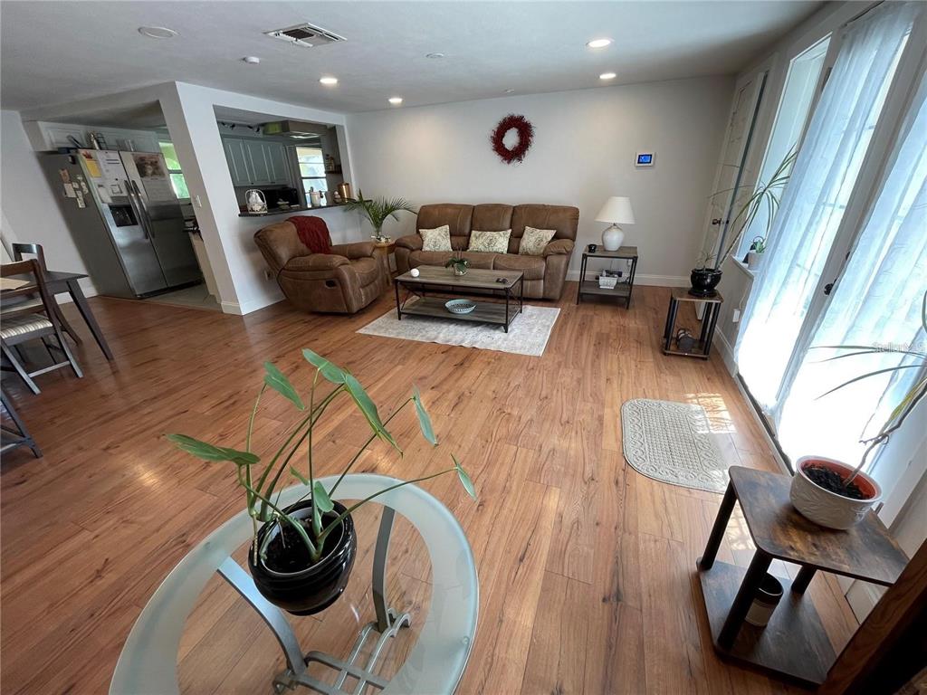A living room with wood-look flooring, a brown sofa, a recliner, and an open kitchen — 5736 COLONIAL DRIVE, NEW PORT RICHEY, FL
