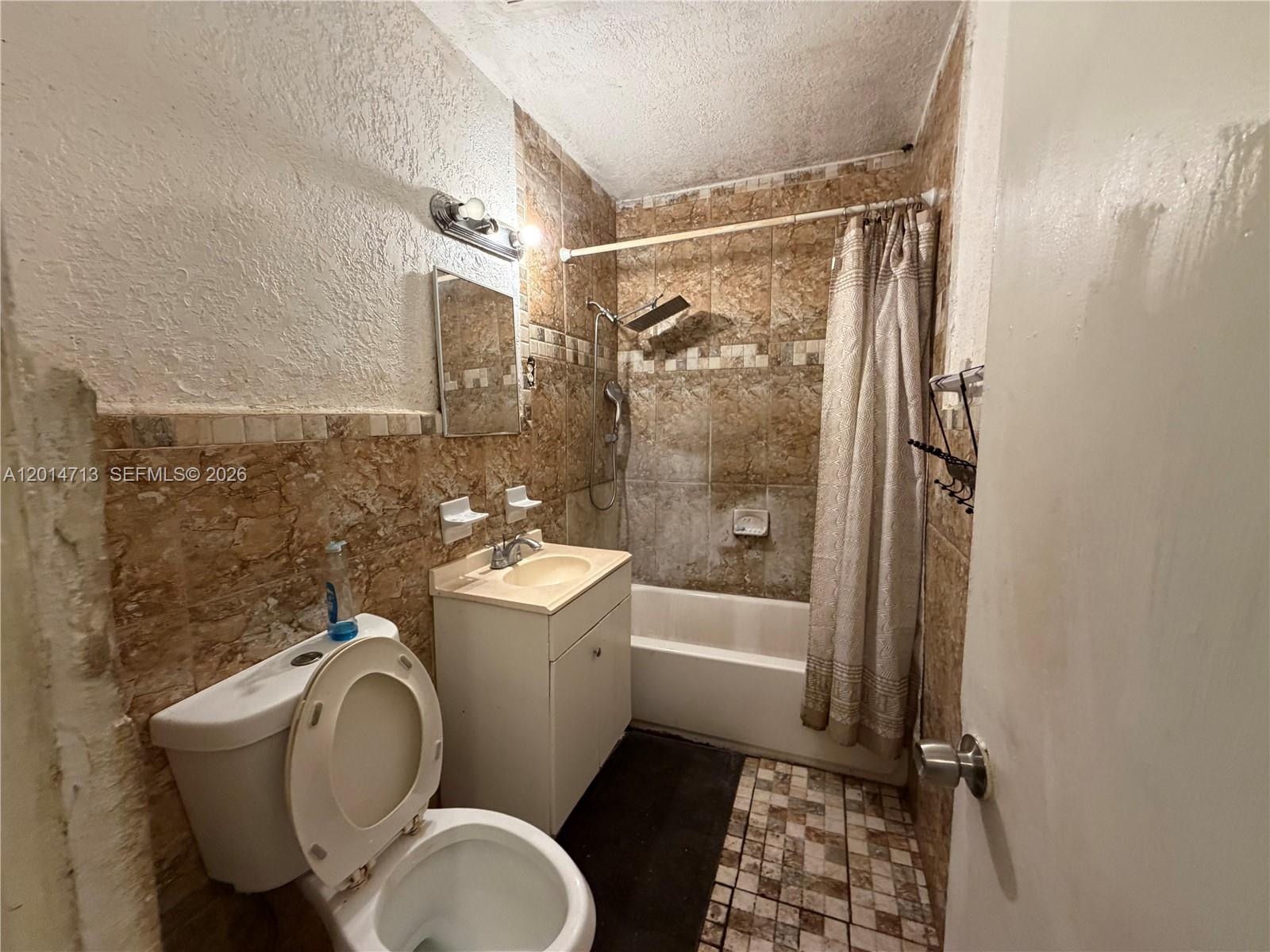 A small bathroom features a toilet, a vanity, and a tub with a shower head — 385 NE 129th St, North Miami FL 33161, NORTH MIAMI, FL