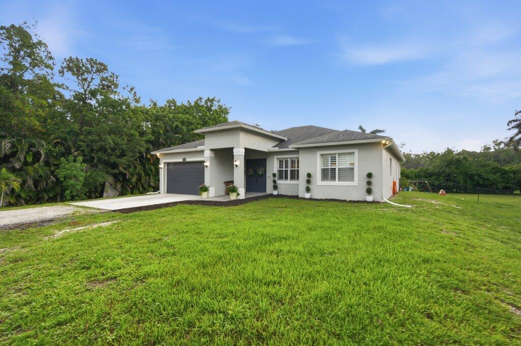 A single-story house with a gray exterior, a dark garage door, and a grassy yard — 18310 42nd Road N, FL 33470, FL