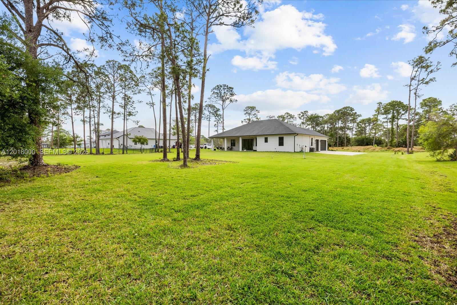 A white house with a dark roof sits on a large, grassy lot with trees — 10630 Sugar Pine Dr, Fort Pierce FL 34945, FORT PIERCE, FL