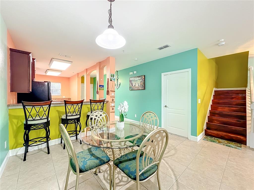 A dining area with a glass table, metal chairs, and a breakfast bar with stools — 10100 GREEN BRANCH COURT, ORLANDO, FL