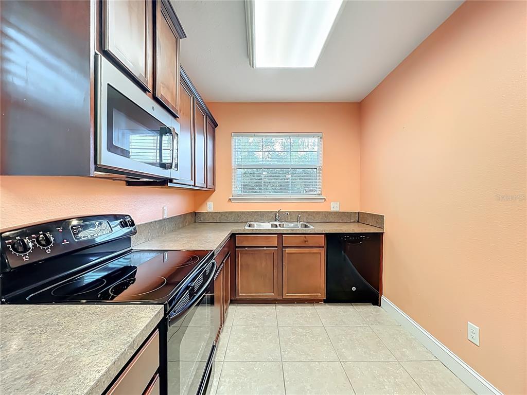 A kitchen features wood cabinets, dark countertops, a black stove, and peach-colored walls — 10100 GREEN BRANCH COURT, ORLANDO, FL