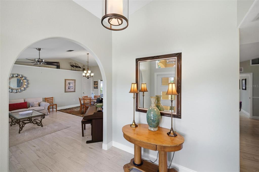 A foyer with a wooden console table and mirror leads through an archway into a living room — 894 BOUNDARY BOULEVARD, ROTONDA WEST, FL