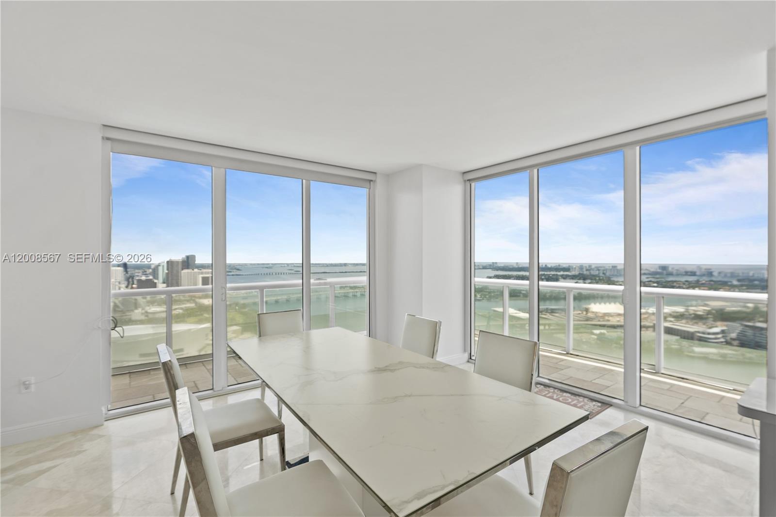 A dining area with a marble table and chairs surrounded by floor-to-ceiling windows — 50 Biscayne Blvd # 5402, Miami FL 33132, MIAMI, FL