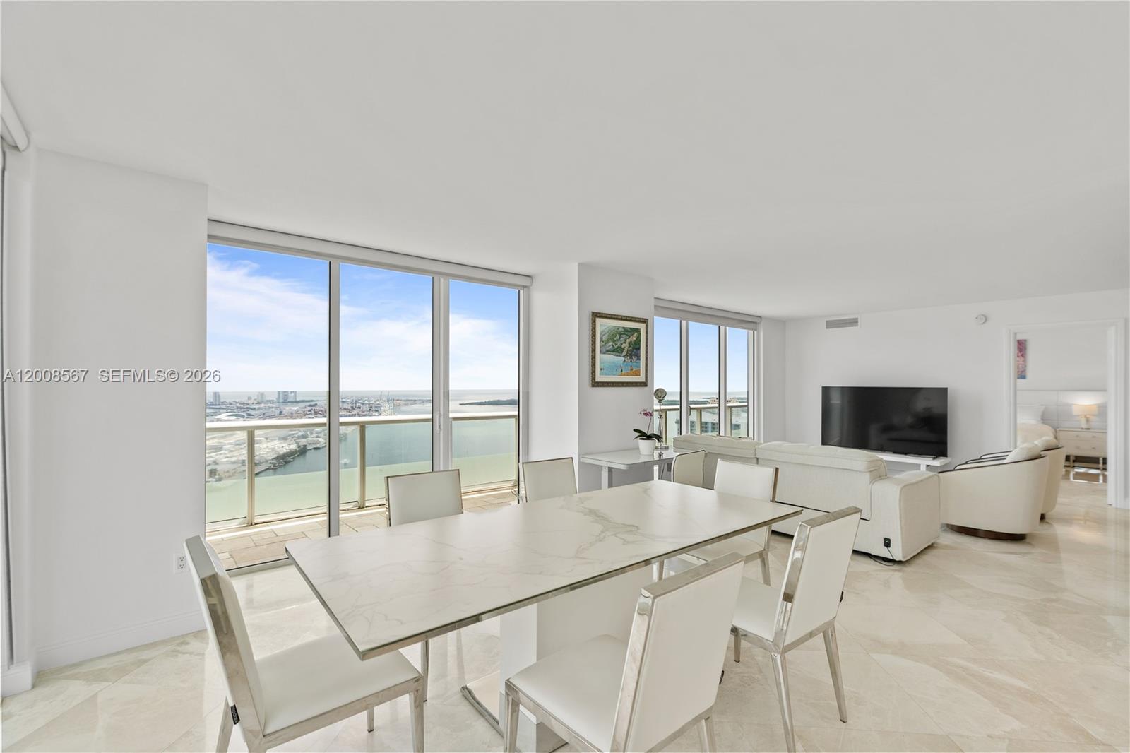 A dining area with a marble table and chairs overlooks a balcony and ocean view — 50 Biscayne Blvd # 5402, Miami FL 33132, MIAMI, FL