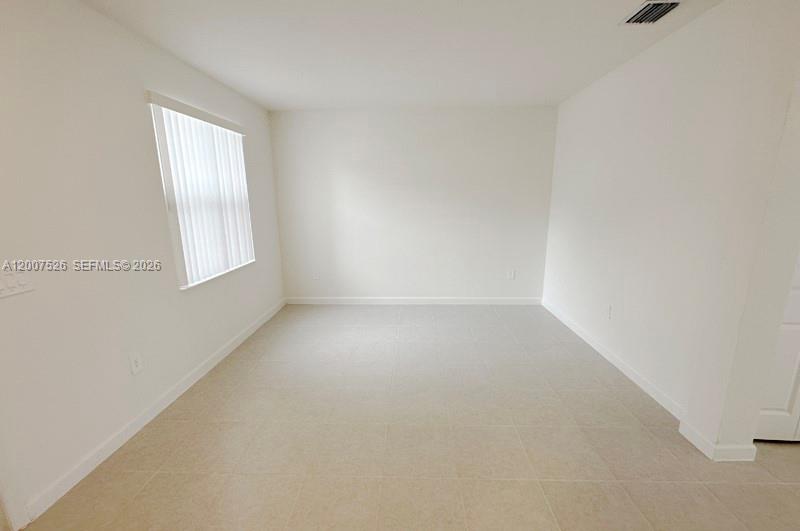 An empty room features white walls, light-colored tile flooring, and a window with blinds — 12428 NW 23rd Ct, Miami FL 33167, MIAMI, FL