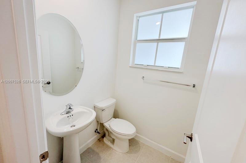 A small bathroom features a pedestal sink, an oval mirror, and a white toilet — 12428 NW 23rd Ct, Miami FL 33167, MIAMI, FL