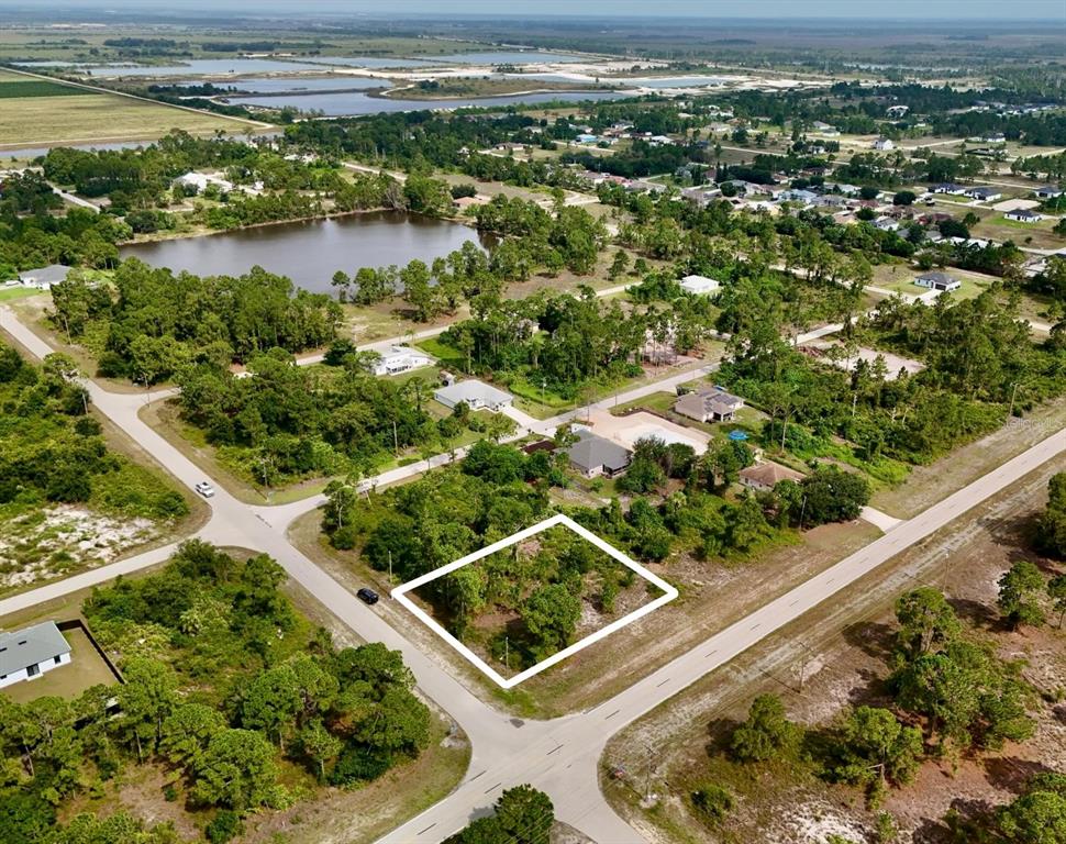 An aerial view shows a vacant, wooded corner lot outlined in white within a residential neighborhood — 1041 COLUMBUS BOULEVARD, LEHIGH ACRES, FL