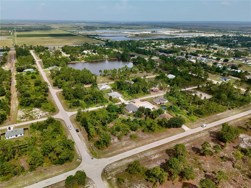An aerial view shows a rural residential neighborhood with scattered houses, trees, and a pond — 1041 COLUMBUS BOULEVARD, LEHIGH ACRES, FL