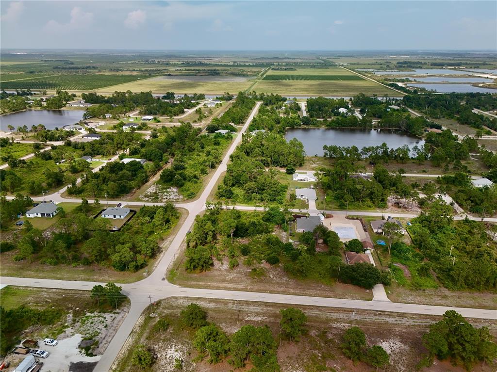 An aerial view shows a rural residential neighborhood with scattered houses, ponds, and surrounding farmland — 1041 COLUMBUS BOULEVARD, LEHIGH ACRES, FL