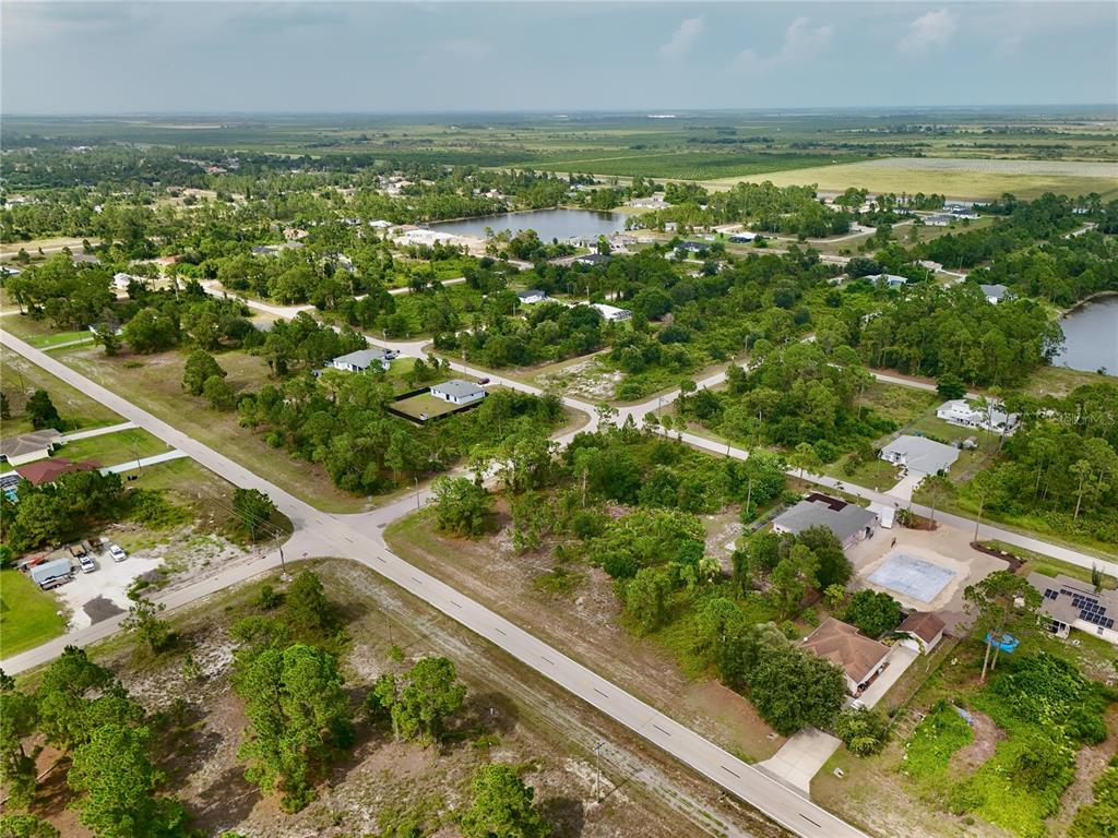 An aerial view shows a rural residential neighborhood with scattered houses, trees, and paved roads — 1041 COLUMBUS BOULEVARD, LEHIGH ACRES, FL