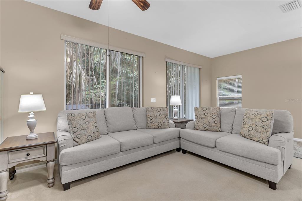 A living room features two light-colored sofas, beige carpeting, and large windows with blinds — 572 PINEBRANCH CIRCLE, WINTER SPRINGS, FL
