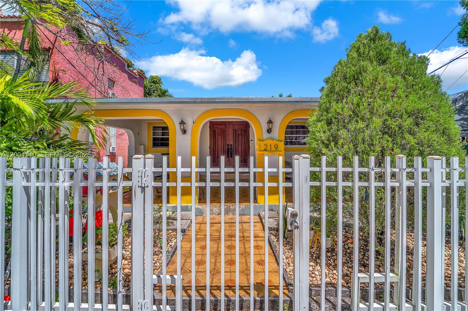 A white house with yellow arched trim and a wooden front door sits behind a fence — 219 SW 6th Ave, Miami FL 33130, MIAMI, FL