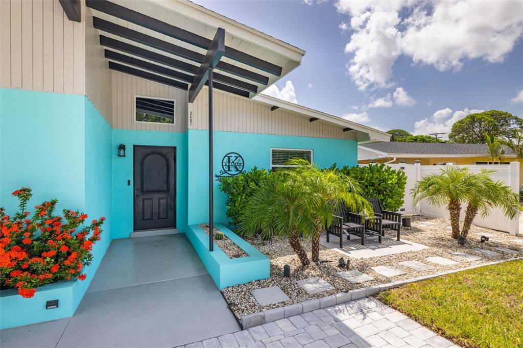 A bright turquoise house exterior features a dark front door, palm trees, and gravel landscaping — 3407 29TH STREET W, BRADENTON, FL
