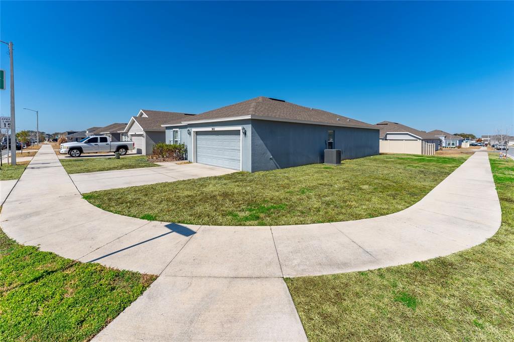 A gray single-story house with a two-car garage sits on a corner lot with sidewalks — 3802 WHITNEY WAY, HAINES CITY, FL