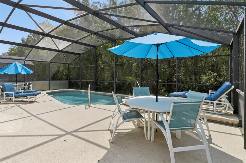 A screened-in pool patio features a dining set, lounge chairs, and two blue umbrellas — 138 MADIERA BEACH BOULEVARD, KISSIMMEE, FL